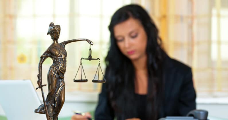 Female lawyer behind scales of justice statue